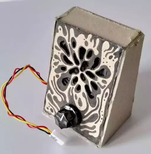 A patterned cardboard box with a volume knob, irregular holes, and a JST connector.
