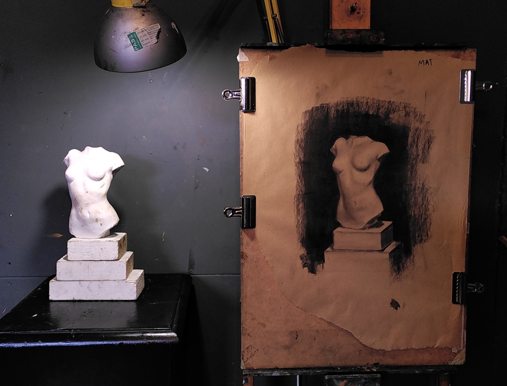 Charcoal drawing on brown packing paper of a lit plaster cast torso bust, beside the real thing.