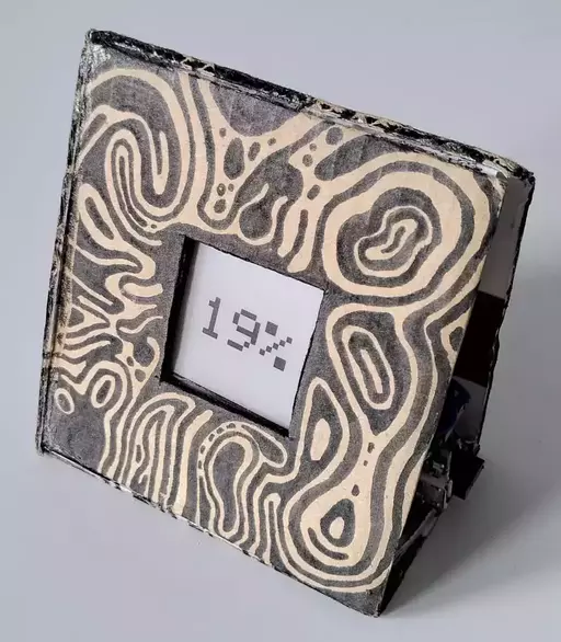A patterned cardboard box with a small E-ink screen displaying a percentage.