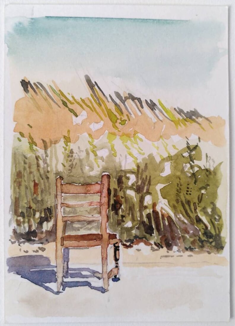 Watercolour painting of a rustic wooden chair on a dirt road, facing a hilly overgrown field of grass.