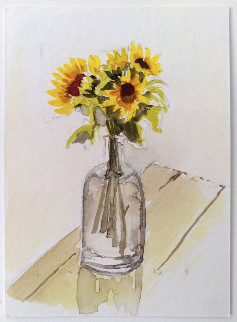 Watercolour painting of sunflowers in a vase of water, on a wooden table. Light shines through the vase from behind.