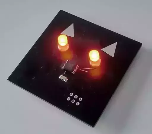 Square PCB designed to look like a cat's face, with red glowing LED eyes.